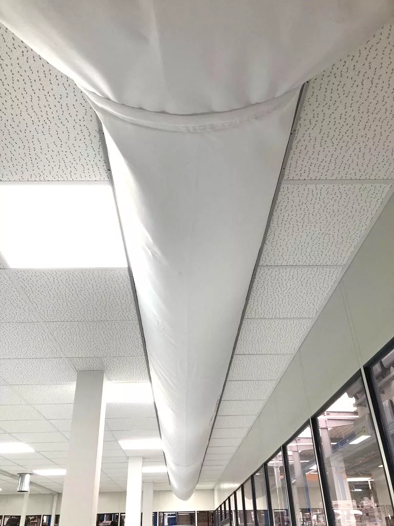 Weißer textilkanal in einem Bürogebäude unter abgehängter Decke zur gleichmäßigen lüftung entlang des Raumes.