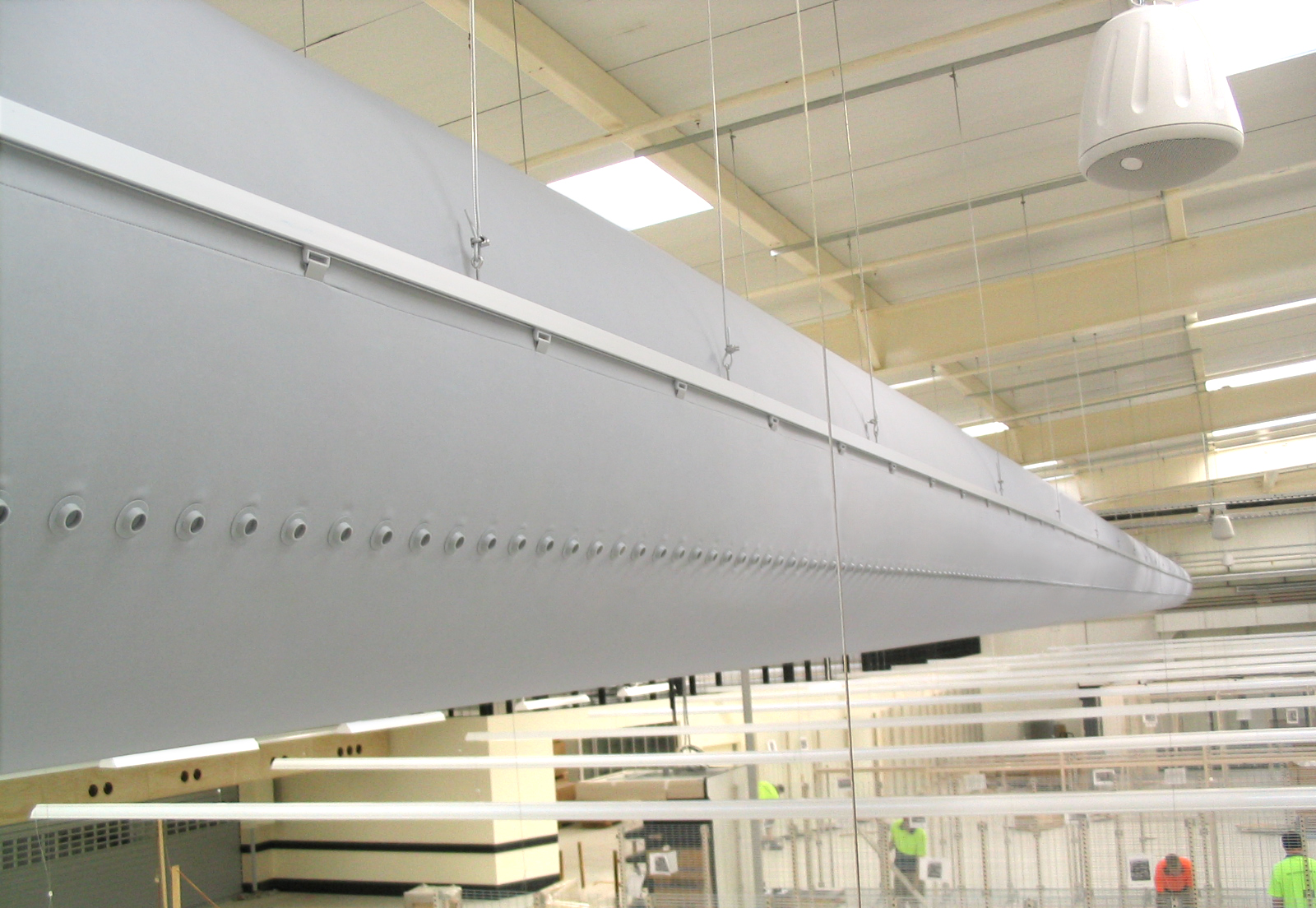 Graues FabricAir Textilluftkanalsystem mit präzisen Luftauslässen in einer industriellen Produktions- oder Montagehalle installiert.