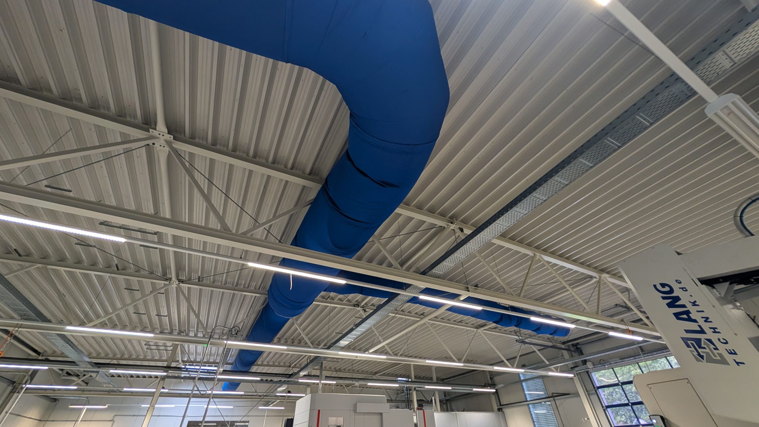 Blaue Textilkanäle von FabricAir installiert in einer Produktionshalle für Sensoren zur gleichmäßigen Luftverteilung.