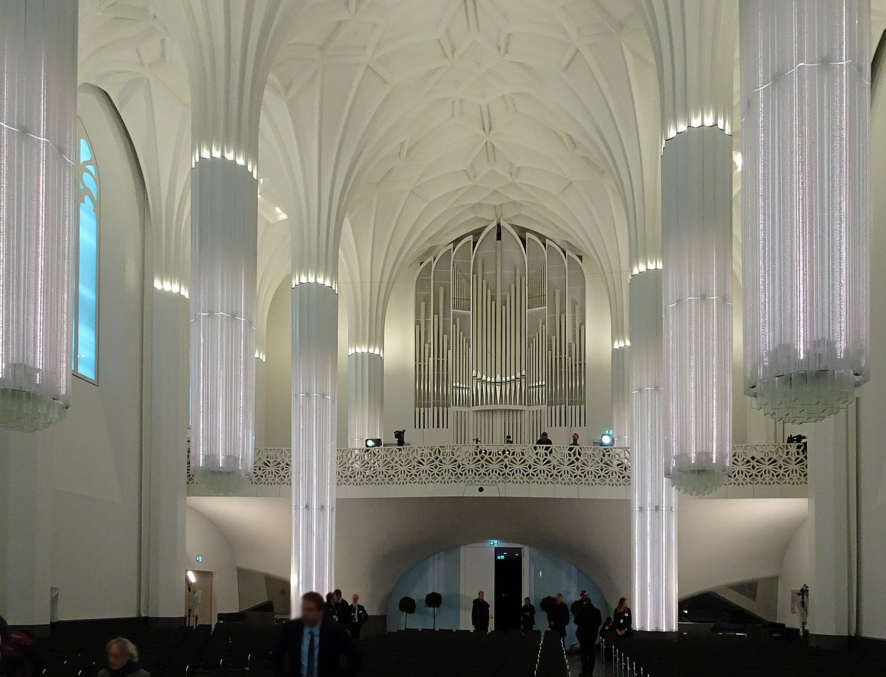 Kathedralartiger Innenraum mit symmetrischen Säulen, vertikalen Leuchtelementen und klarer, lichtdurchfluteter Architektur.
