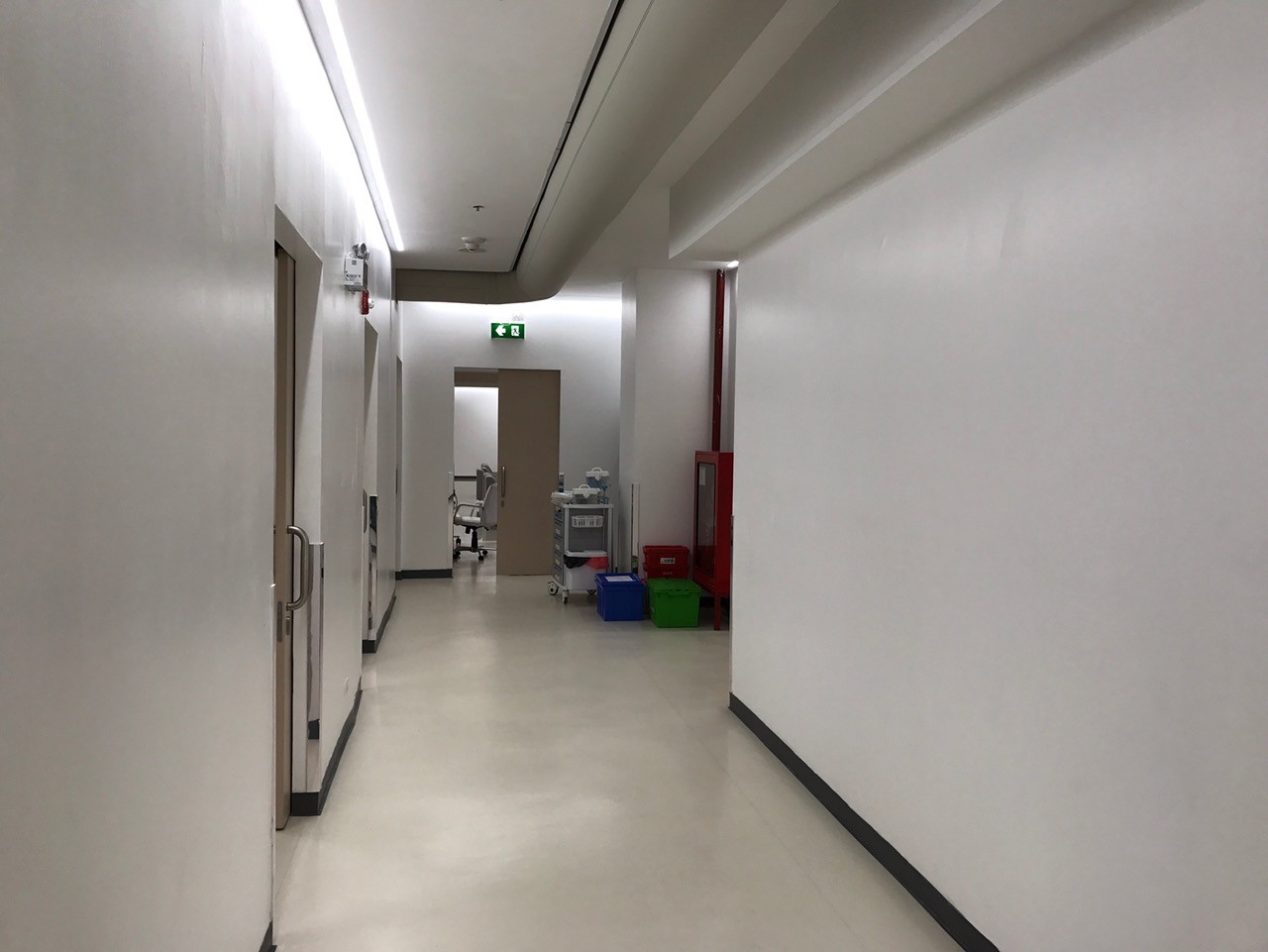 Schmaler Klinikflur mit funktionaler Ausstattung, medizinischen Wagen und dezent geführtem Deckensystem für die Luftverteilung.