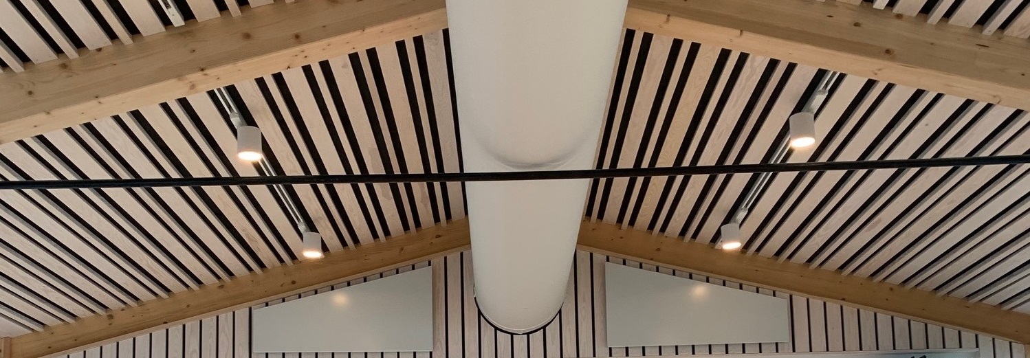 Architektonische Holzdecke mit zentral integriertem Textilluftkanal und linearem Akustik-Lamellendesign.
