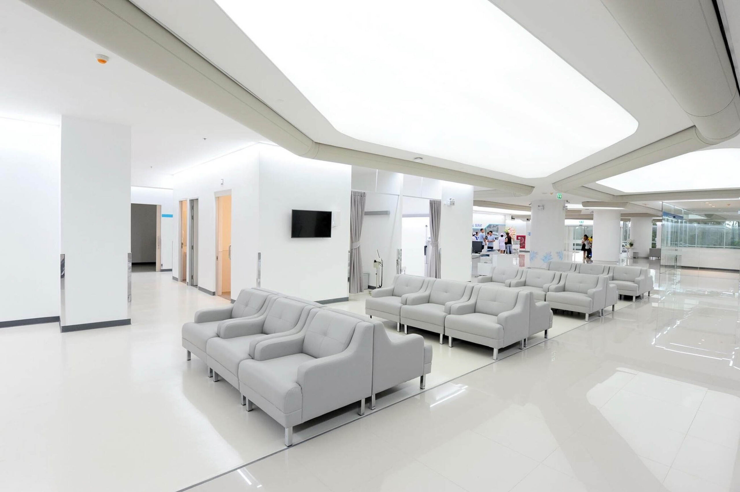 Minimalistischer Krankenhaus-Wartebereich mit integrierter geschwungener Deckenbeleuchtung und modernen Lounge-Sitzmöbeln.