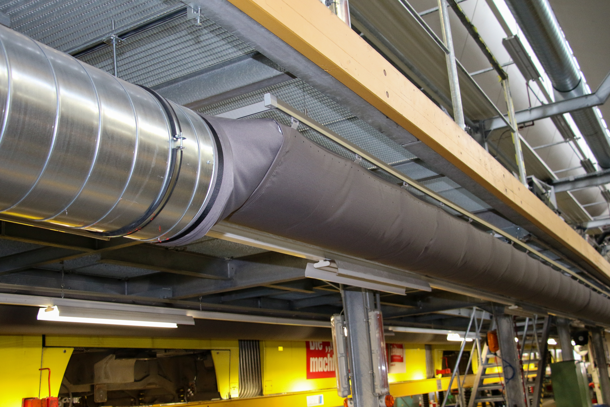 Industriehalle mit Übergang von Metallkanälen zu textilen Luftkanälen unterhalb der Tragkonstruktion.