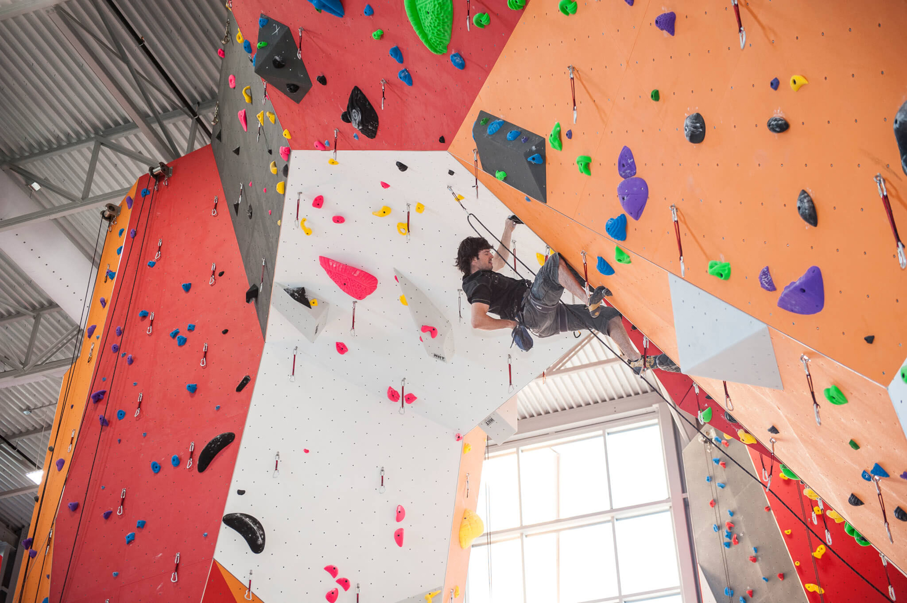 Indoor-Kletterhalle mit farbigen künstlichen Kletterwänden und abgehängten Textilluftkanälen innerhalb der Deckenkonstruktion.