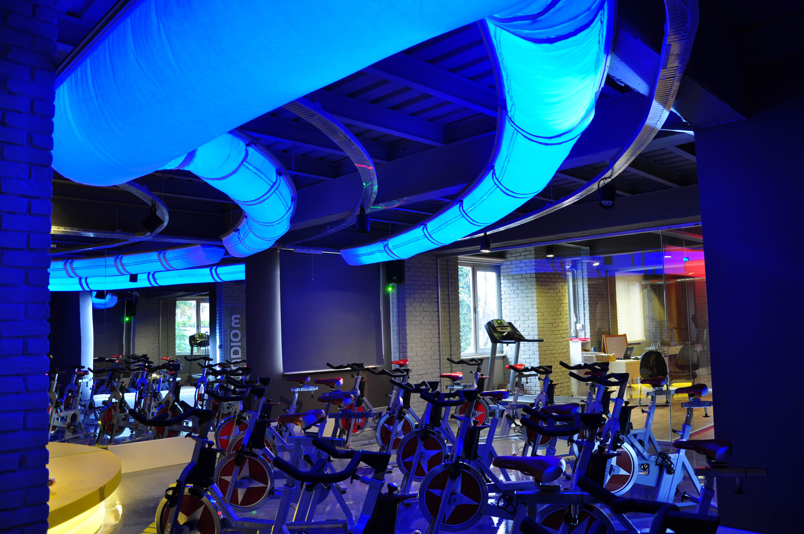 Modernes Fitnessstudio mit beleuchteten Textilluftkanälen innerhalb der Deckenkonstruktion oberhalb der Trainingsgeräte.