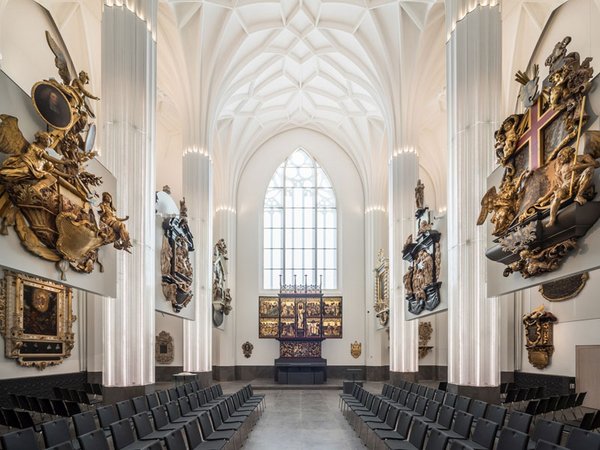 Historischer Kircheninnenraum mit gotischem Gewölbe, dekorativen Wandskulpturen und vertikalen beleuchteten Architekturelementen.