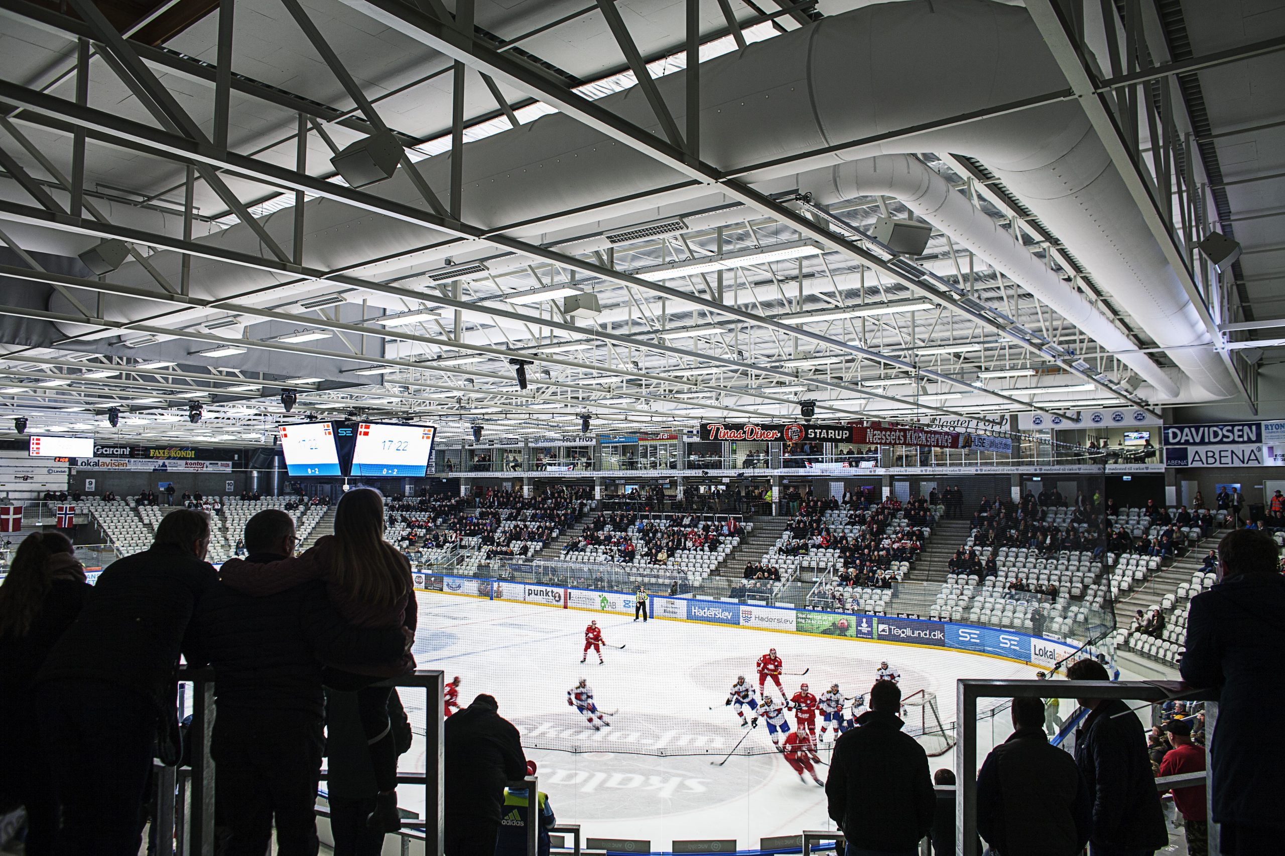 Innenraum eines Eishockeystadions mit abgehängten weißen Textilluftkanälen innerhalb der offenen Stahl-Deckenkonstruktion.