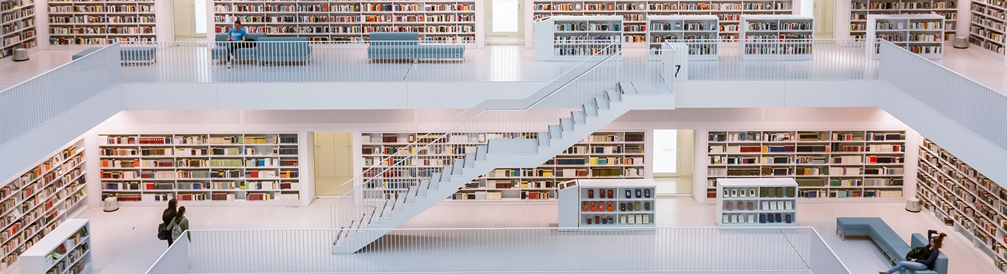 Heller Bibliotheksraum mit Bücherregalen und zentraler Treppe.