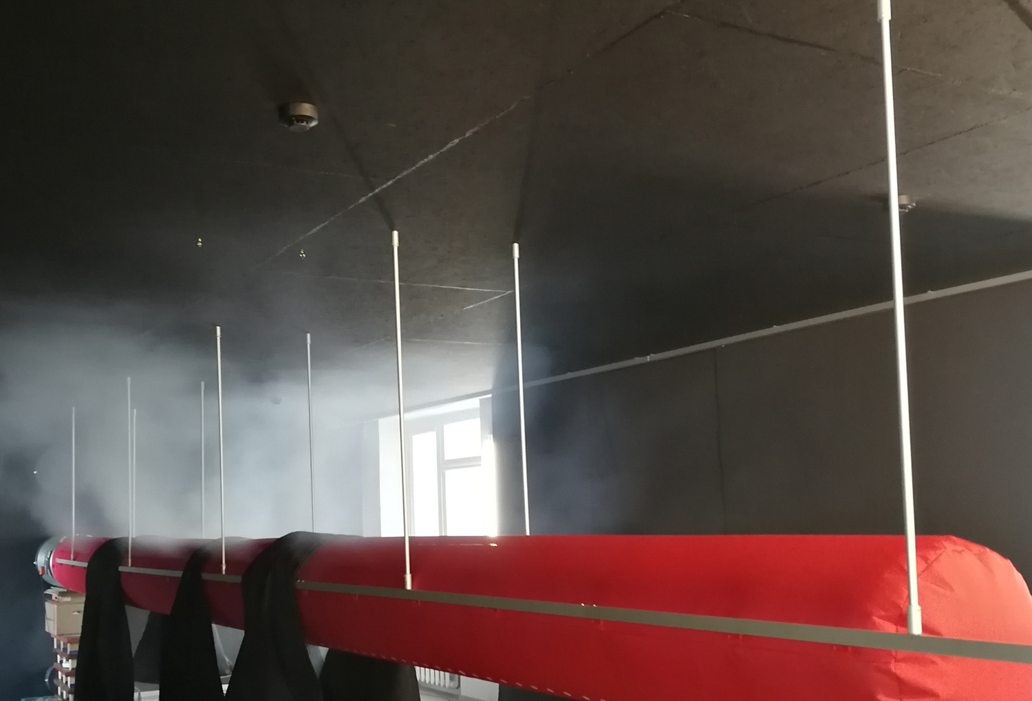 Red air duct system with red fabric ducts inside a foggy room, UK, 2