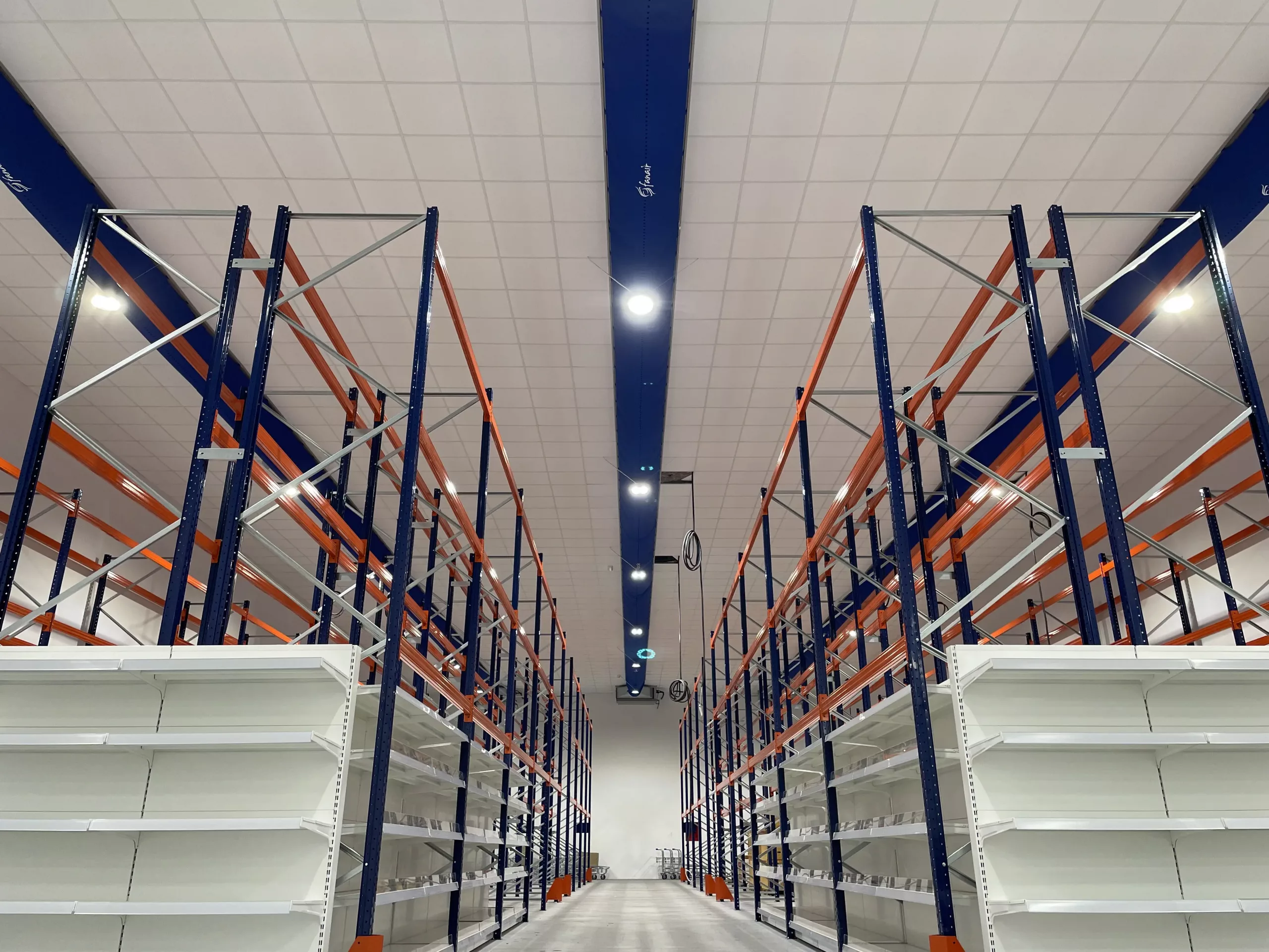 Fabric duct installed in Fanair Warehouse showroom featuring bright blue Combi 90 D-shaped/semi-circular fabric duct with custom heat transferred logos above display racks.