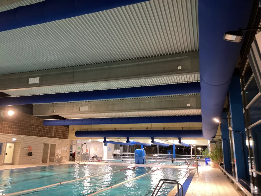 FabricAir’s innovative fabric HVAC solution installed in indoor swimming facility, blue fabric duct suspended over swimming pools