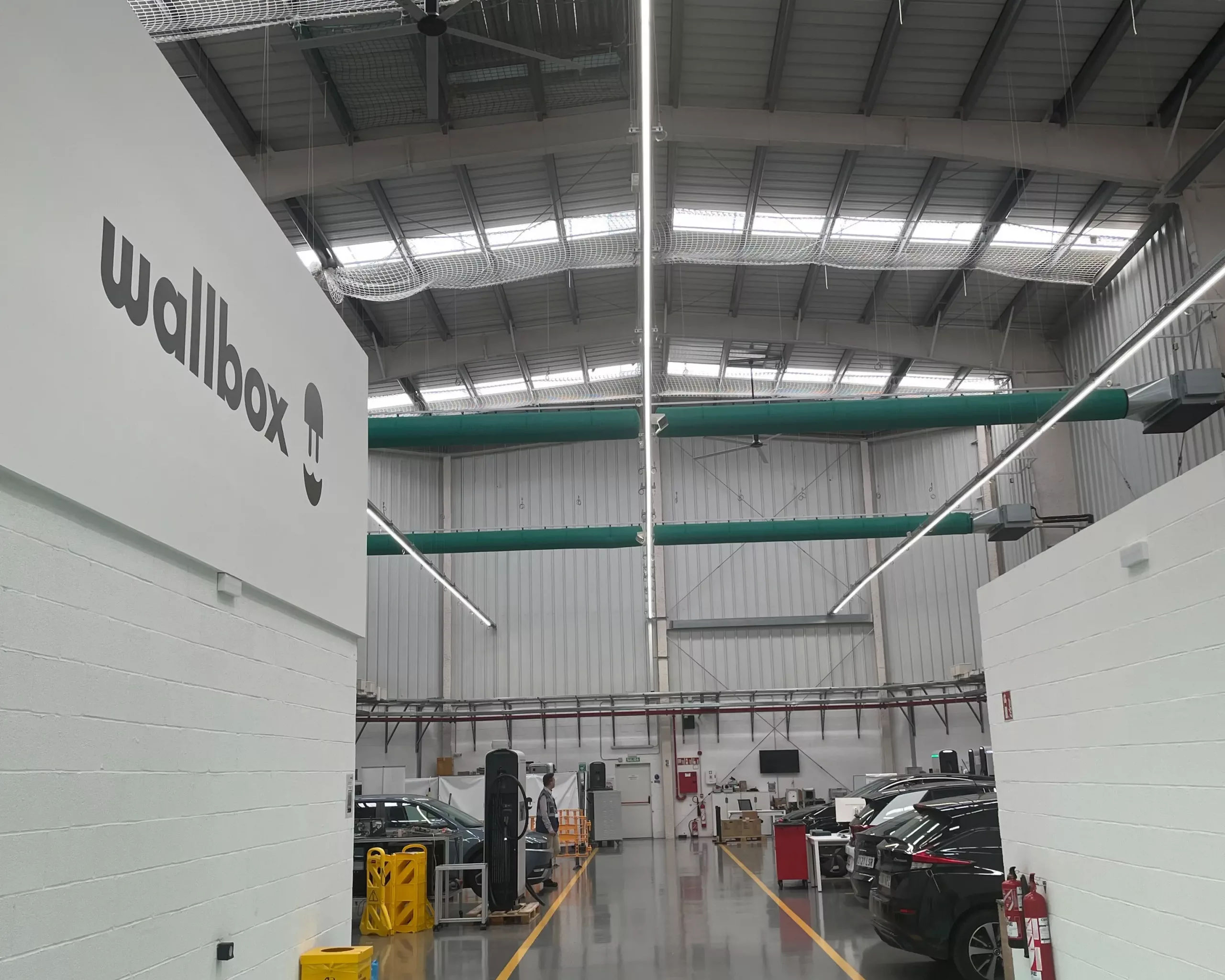 A fabric-based air distribution system installed in the Wallbox warehouse in Barcelona, Spain featuring green Combi 70 FabricAir cleanroom grade fabric with SonicFlow and FabFlow diffusion models. The system ensures clean comfortable, draft free airflow to the industrial workspace.