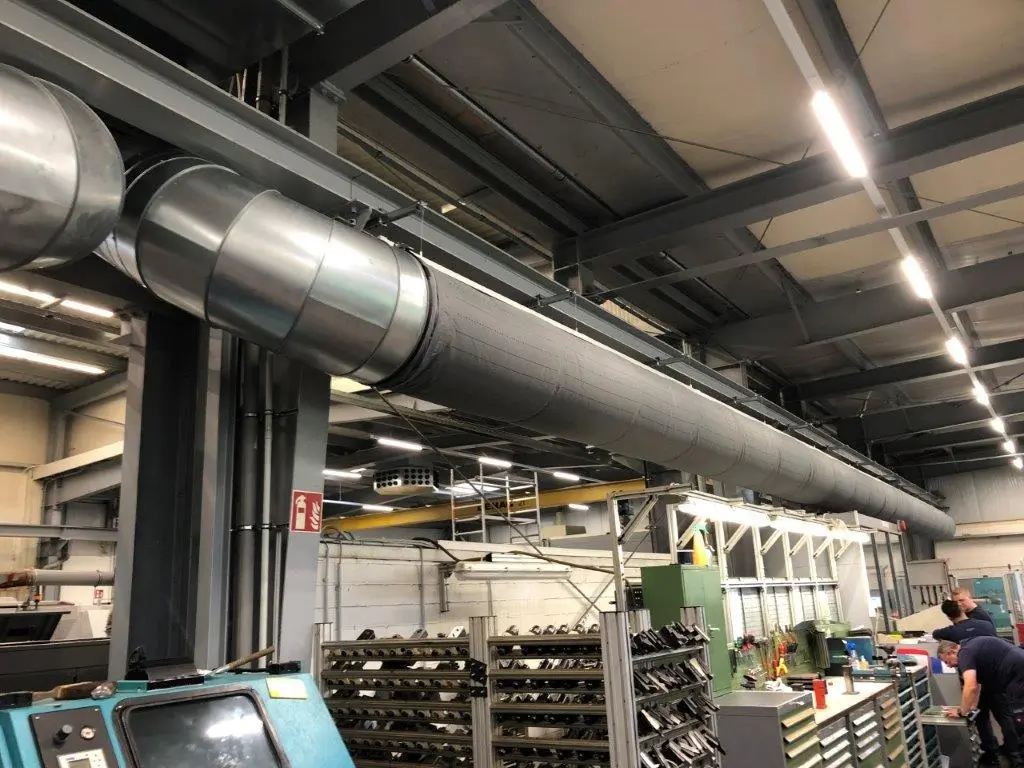 Dark gray fabric ducts are installed using the Type 08 suspension package in this industrial manufacturing facility to ensure temperature control in production areas and provide high quality airflow for employees.