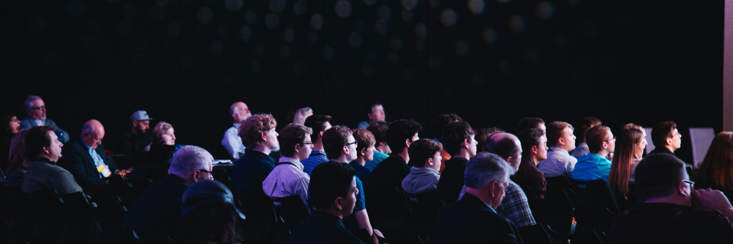 Audience seated in a darkened conference hall watching a presentation