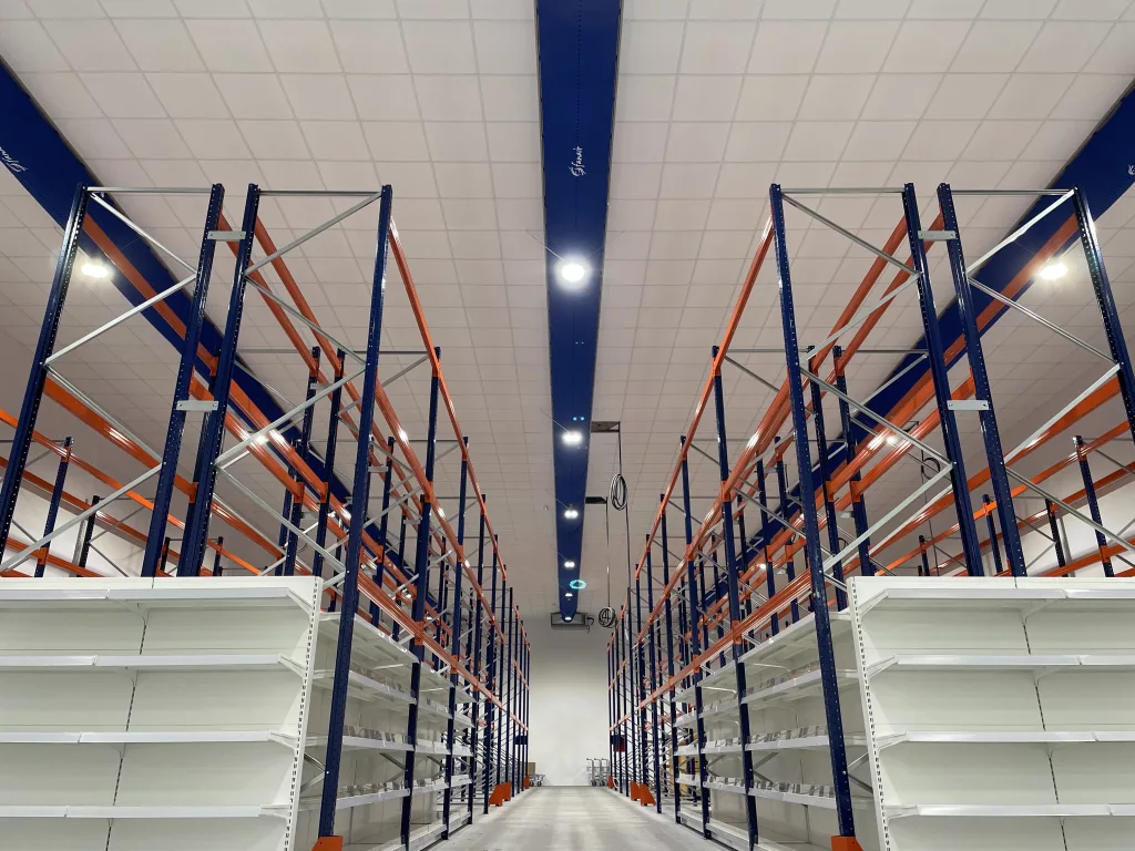 Fabric duct installed in Fanair Warehouse showroom featuring bright blue Combi 90 D-shaped/semi-circular fabric duct with custom heat transferred logos above display racks.