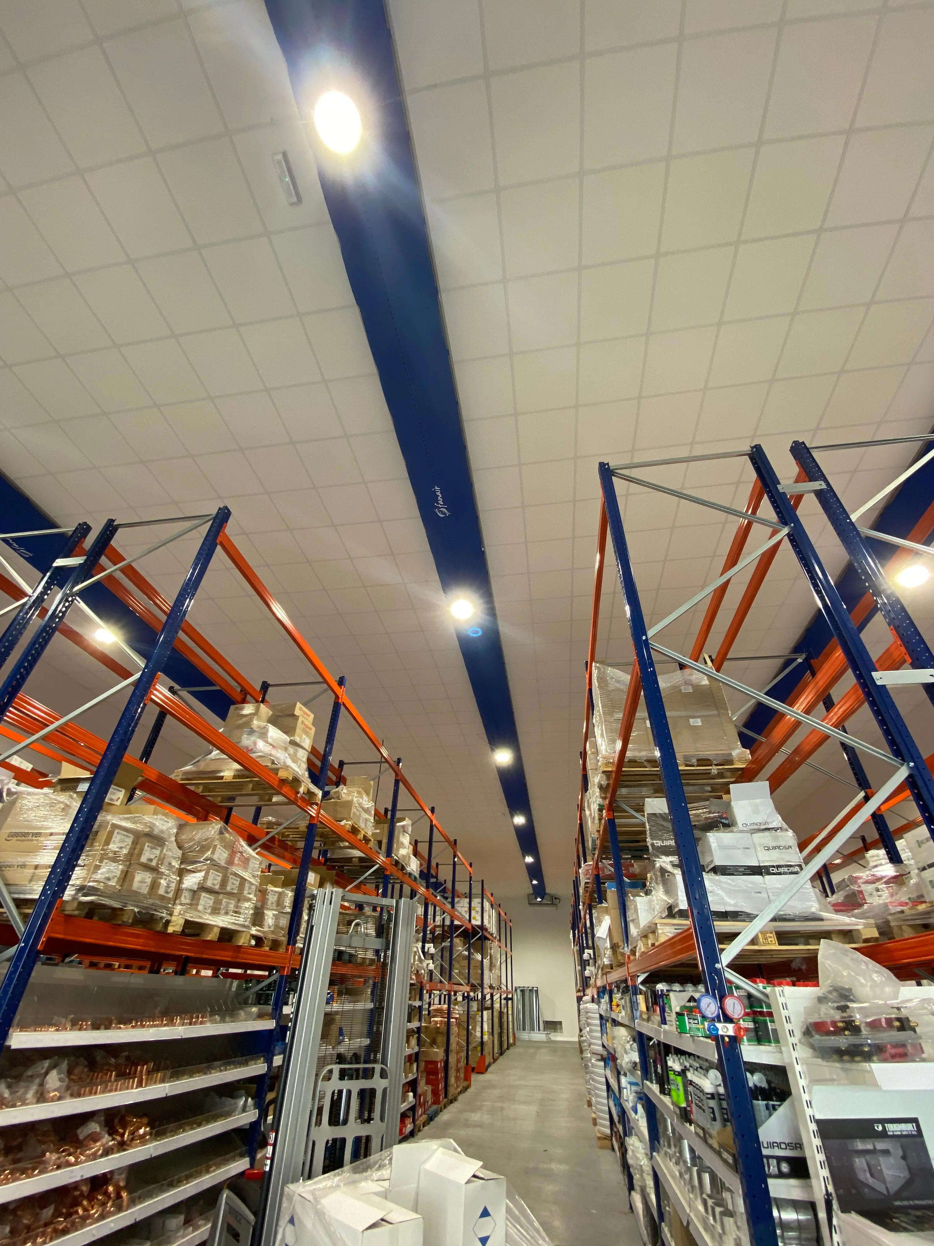 Fabric duct installed in Fanair Warehouse showroom featuring bright blue Combi 90 D-shaped/semi-circular fabric duct with custom heat transferred logos above display racks.