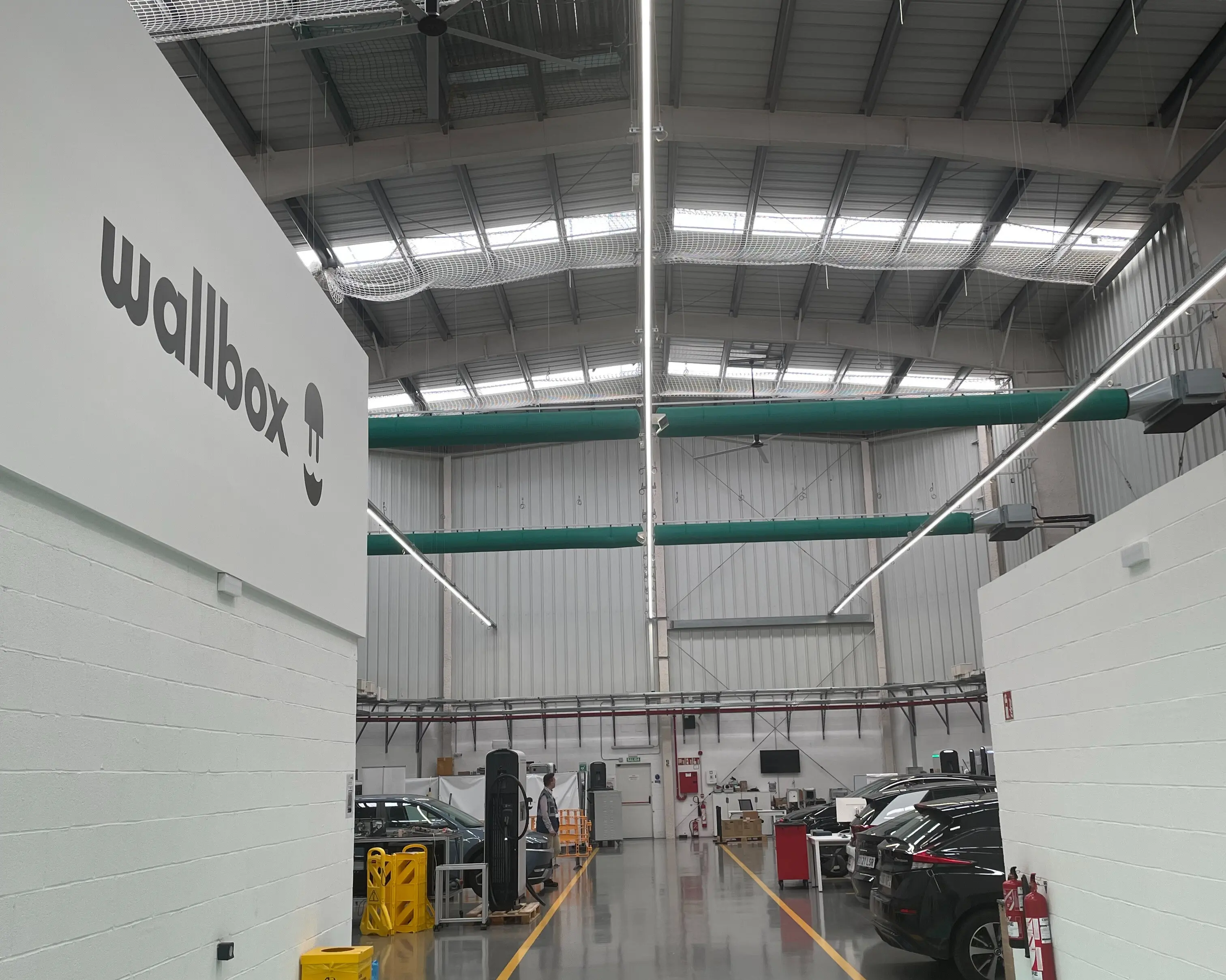 A fabric-based air distribution system installed in the Wallbox warehouse in Barcelona, Spain featuring green Combi 70 FabricAir cleanroom grade fabric with SonicFlow and FabFlow diffusion models. The system ensures clean comfortable, draft free airflow to the industrial workspace.
