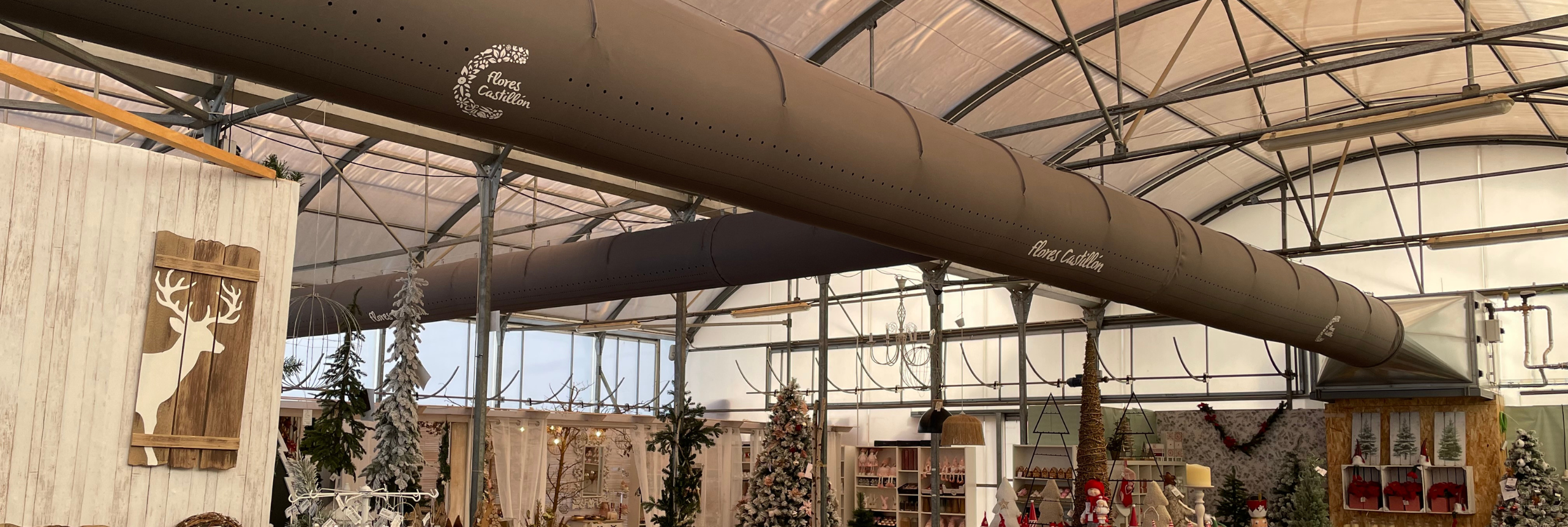 FabricAir ducts in gray fabric featuring custom logos and All-In-One duct shape retention are installed in the Flores Castillon greenhouse and nursery in Barbastro, Spain.