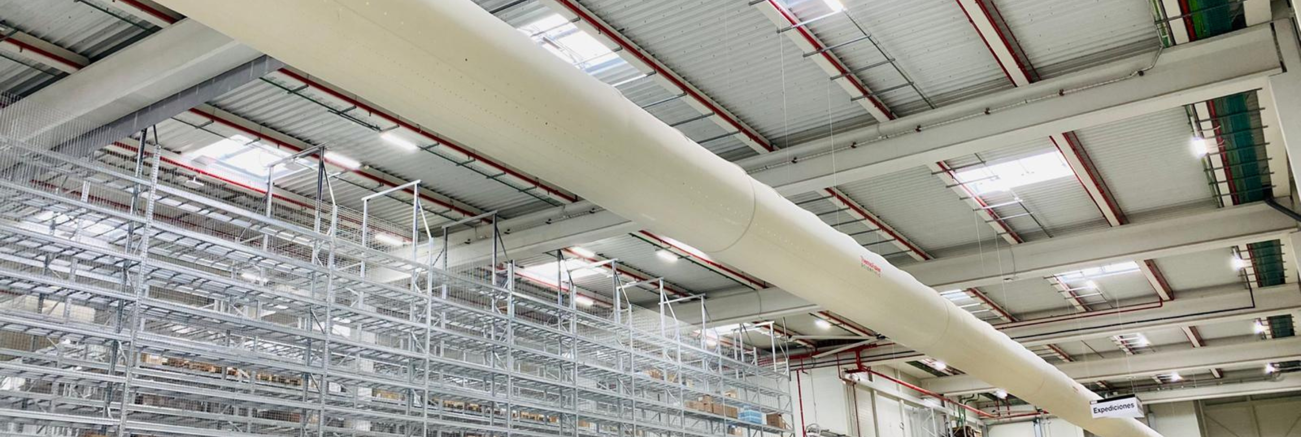 White FabricAir ducts featuring the Thermo Fisher logo are installed in a warehouse in Barcelona Spain to provide precise, uniform airflow without the risk of condensation.