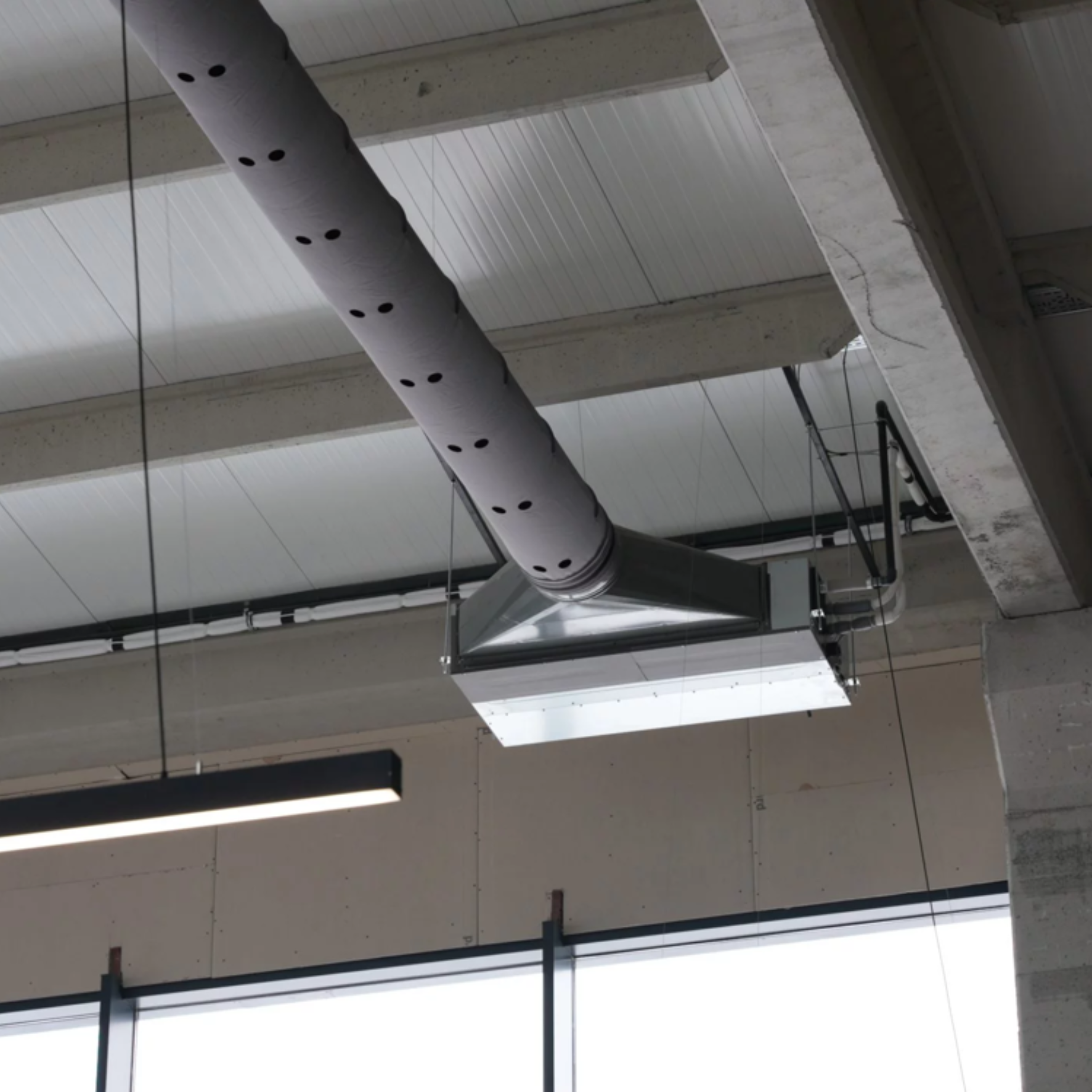 Gray fabric ducts with custom-engineered airflow through laser cut holes provide optimal comfort in an automotive showroom with high ceilings