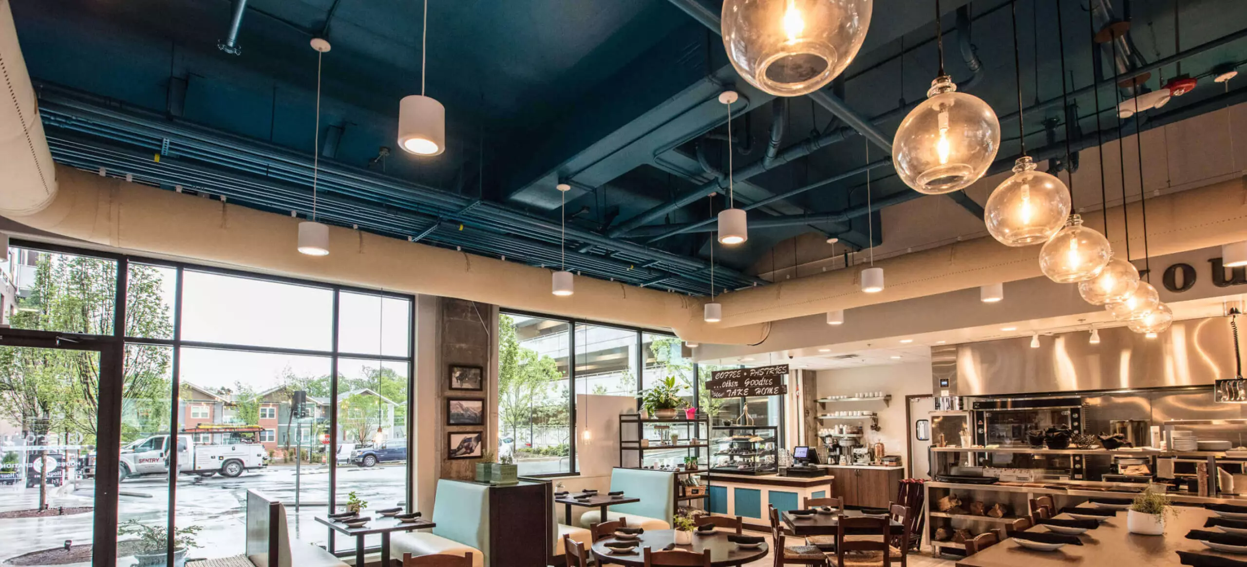 Modern cafe interior with large windows, dining tables, pendant lights, and a pastry display counter.